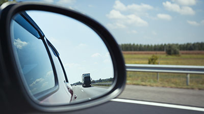 Close up of a car rear-view mirror, in the mirror you can see an large truck driving on a road.