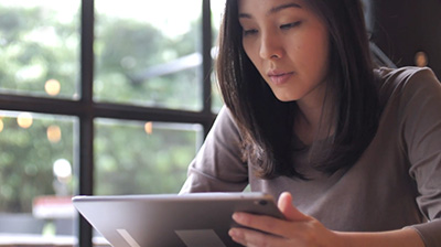 A woman using a tablet while sitting next to a window 