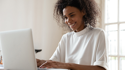 A woman in a white blouse, smiling while using her laptop 