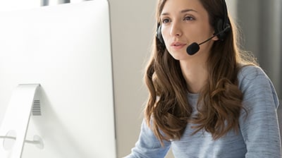 A woman with a headset on while using her computer 