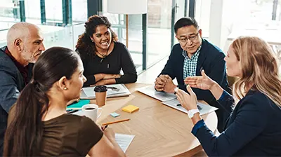 Three business women and two business men smiling while having a conversation at a round table