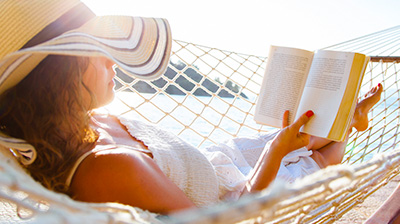 Woman with a sun hat reading a book while laying in a hammock
