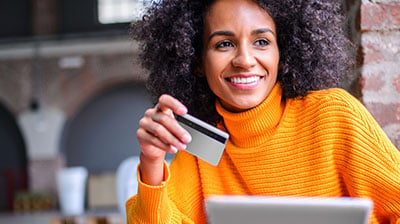 A woman in an orange turtleneck sweater smiling while holding a credit card in her hand
