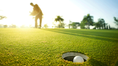A man's silhouette in the background hitting a golf ball into the hole 