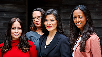 Four women dressed in business attire standing next to each other while slightly smiling 