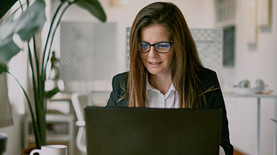 A woman wearing glasses and looking down at her laptop 