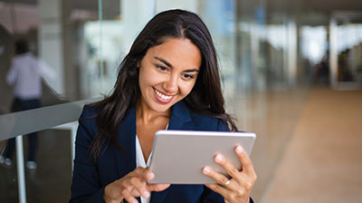 A woman in business attire smiling at a tablet while holding it with both hands