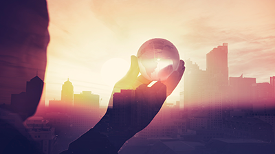 Silhouette of a man holding a glass ball up to a city skyline with the sun shining through the buildings 