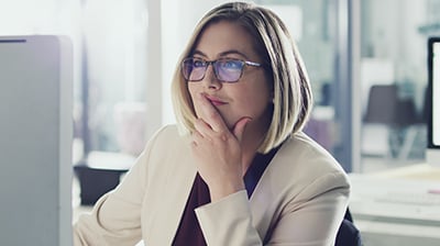 A businesswoman wearing glasses, working on a desktop computer