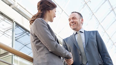 A man and a woman, both wearing suits, shaking hands 