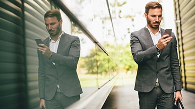 A man in a suit standing outside while using his phone 